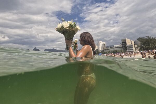 فتاة تضع الزهور في مياه شاطئ أربوادور كقرابين خلال احتفال سنوي لتكريم ييمانجا، إلهة البحر الأفريقية، في ريو دي جانيرو.  - سبوتنيك عربي