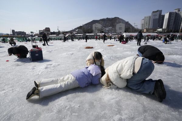 أحد أفراد الأسرة يلقي بخط صيد عبر ثقب محفور في سطح نهر متجمد أثناء مسابقة صيد سمك السلمون المرقط في هواتشيون، كوريا الجنوبية.  - سبوتنيك عربي