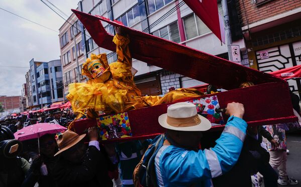 رجل يرتدي زي بيبينو التقليدي يستلقي داخل نعش محمول على أكتاف بعض المشاركين في المهرجان. - سبوتنيك عربي