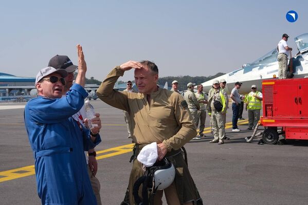 طيارون وفنيو طيران يتحدوثون خلال فعاليات المعرض، وفي الخلف فنيون يقفون إلى جانب مقاتلة روسية - سبوتنيك عربي