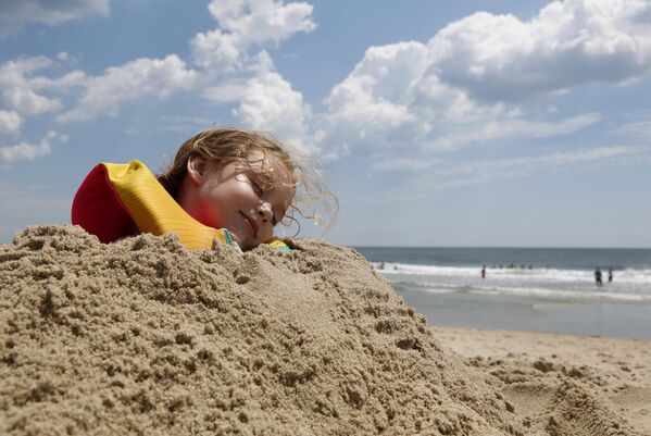 طفلة تتظاهر بالنوم بعد أن غطاها والدها بالرمل على الشاطئ في أمريكا  - سبوتنيك عربي