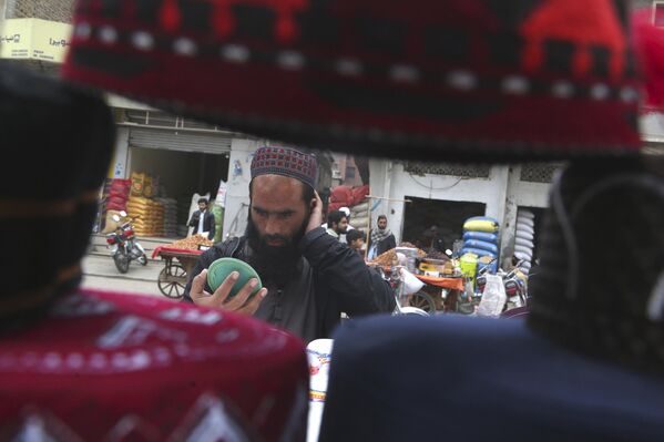رجل يجرب قبعة تقليدية لاستخدامها أثناء الصلاة خلال شهر رمضان، في أحد الأكشاك في بيشاور، باكستان. - سبوتنيك عربي