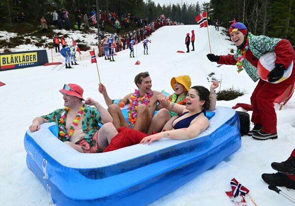 طلاب نرويجيون يرتدون ملابس السباحة، ويشاهدون سباقا للتزلج أثناء جلوسهم في حوض سباحة قابل للنفخ في النرويج - سبوتنيك عربي