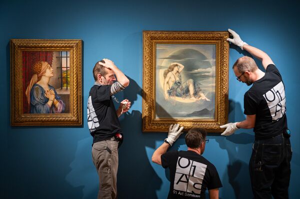 يُجري مُختصّو الفنون تعديلات على لوحتي إيفلين دي مورغان، "لونا"، 1885، زيت على قماش (يمين) وإيفلين دي مورغان، السجينة، 1907-1908، زيت على قماش (يسار) في معرض "جيلدهول" للفنون في 18 مارس 2025 في لندن، إنجلترا. - سبوتنيك عربي