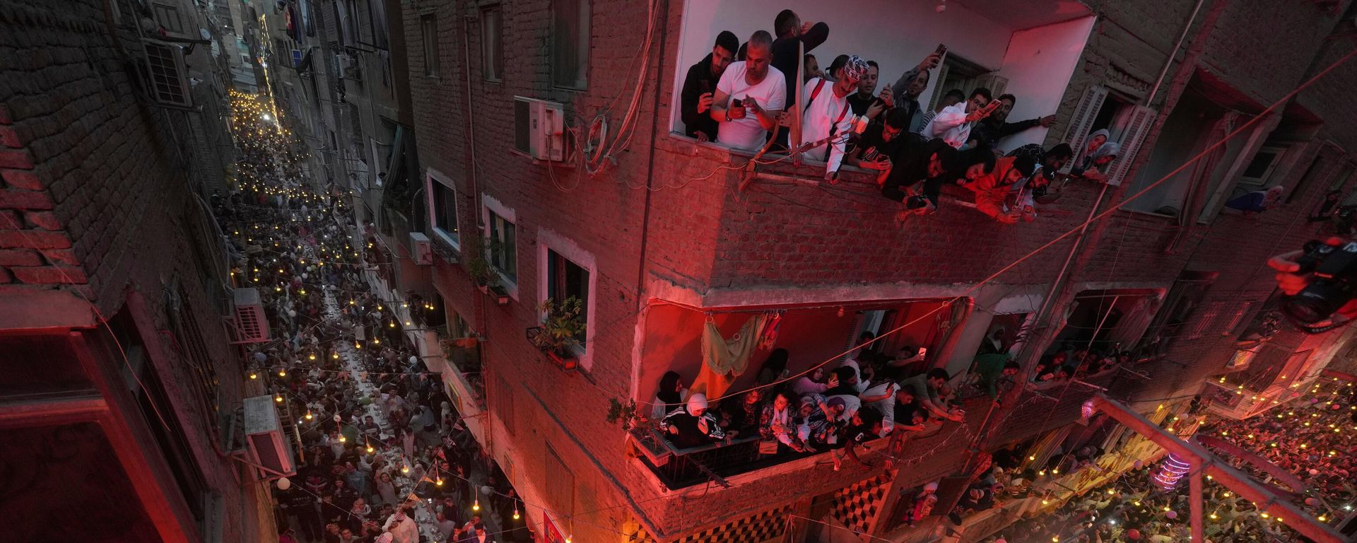 سكان عزبة حمادة في حي المطرية بالقاهرة يطلون من شرفاتهم للاحتفال بإفطار جماعي، وهو الوجبة التي يختتمون بها صيامهم عند غروب الشمس، خلال شهر رمضان المبارك في القاهرة، مصر، السبت 15 مارس/آذار 2025. - سبوتنيك عربي, 1920, 03.08.2026
