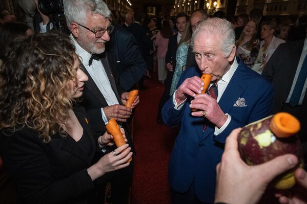 الملك تشارلز الثالث يعزف على آلة موسيقية مصنوعة من الجزر، مع "أوركسترا لندن للخضراوات" خلال حفل استقبال لتكريم المشاركين في الموسيقى المجتمعية في جميع أنحاء المملكة المتحدة. - سبوتنيك عربي