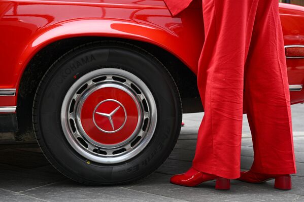 سيارة حمراء تقف صاحبتها بجانبها، مرتدية لباسا بذات لون سيارتها، في التجمع السنوي للسيارات الكلاسيكية على أراضي مجمع التسوق "أرخانغيلسكوي أوتليت" - سبوتنيك عربي