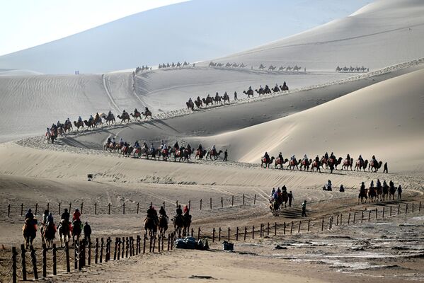 سياح يمتطون الجمال ويزورون جبل "مينغشا" وموقع ا"لهلال الربيعي" الخلاب، في دونهوانغ، مقاطعة غانسو، الصين - سبوتنيك عربي