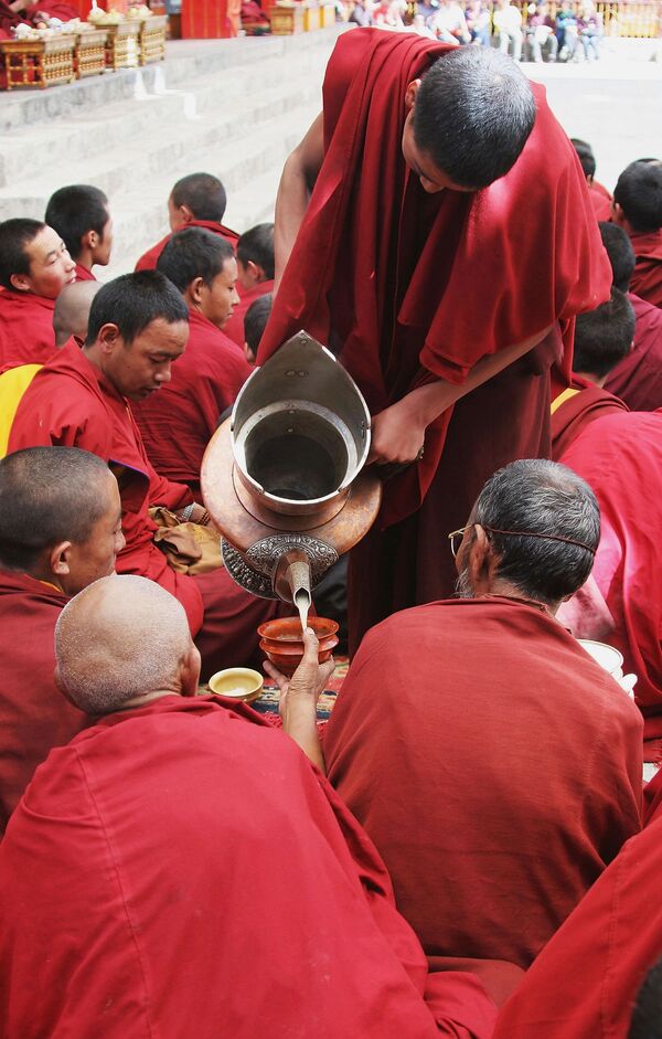 مجموعة دينية من البوذيين تحتسي شاي الزبدة، أثناء حضورهم عرضًا لرقصة دينية في دير تاشيلهونبو في التبت، الصين. - سبوتنيك عربي