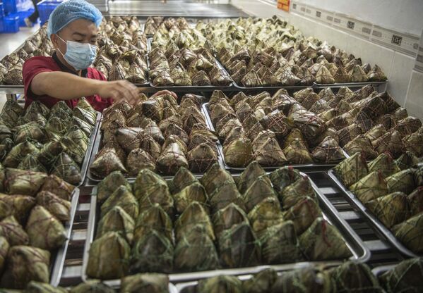 يقوم أحد العمال بترتيب الزلابية التقليدية المصنوعة من الأرز والمغطاة بأوراق الخيزران استعدادًا لمهرجان قوارب التنين في مقاطعة غوانغدونغ الصينية - سبوتنيك عربي