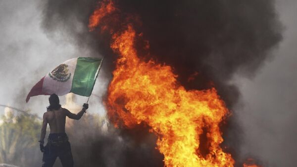 Протестующий машет мексиканским флагом на фоне горящего автомобиля - سبوتنيك عربي
