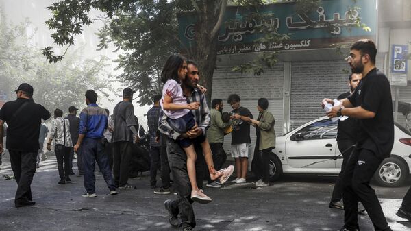 رجل يحمل فتاة مصابة بعد انفجار في وسط طهران جراء الضربات الإسرائيليىة على إيران. - سبوتنيك عربي