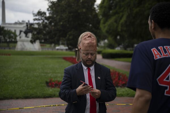 رجل يرتدي قناع ترامب خارج البيت الأبيض خلال مراسم رفع العلم لعمود العلم الذي تم تركيبه حديثًا على الحديقة الشمالية للبيت الأبيض في واشنطن العاصمة، الولايات المتحدة، في 18 يونيو/حزيران 2025. - سبوتنيك عربي