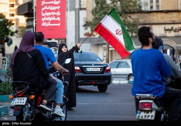 سيدة إيرانية تلوّح بعلم إيران وسط شارع في العاصمة طهران - سبوتنيك عربي
