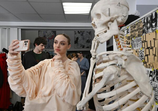 عارضة أزياء تلتقط صورة إلى جانب  هيكل عظمي،  قبل انطلاق عروض مجموعات الدبلوم في معهد إدارة الأعمال والتصميم في موسكو.  - سبوتنيك عربي