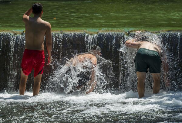شبان يرشون أجسامهم بالمياه في جدول آيسباخ في "الحديقة الإنجليزية" لتبريد أجسامهم من حرارة الشمس. - سبوتنيك عربي