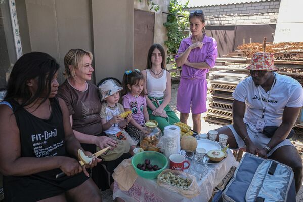 متطوعون من أفريقيا  يجلسون مع عائلة من سكان مدينة ميليتوبول ويتناولون الفواكهه، ضمن المشروع الإنساني الدولي "متطوعو السلام" لتقديم الدعم لكبار السن والأسر الكبيرة في مقاطعة زابوروجيه. - سبوتنيك عربي