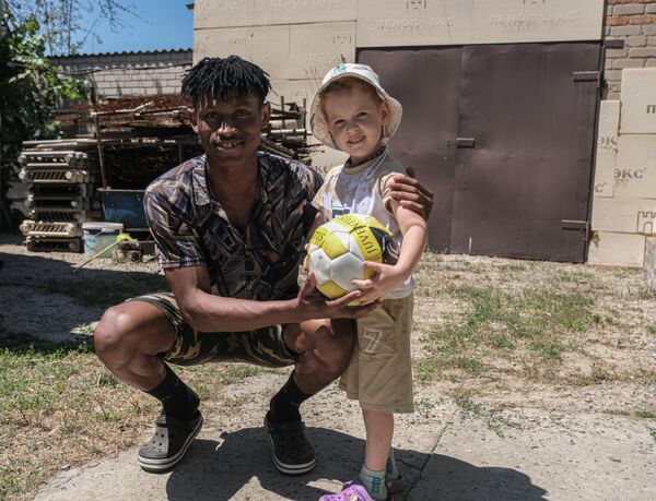 متطوع أفريقي يلتقط صورة مع طفل من مدينة ميليتوبول في مقاطعة زابوروجيه، ضمن المشروع الإنساني الدولي "متطوعو السلام" لتقديم الدعم لكبار السن والأسر الكبيرة في مقاطعة زابوروجيه. - سبوتنيك عربي