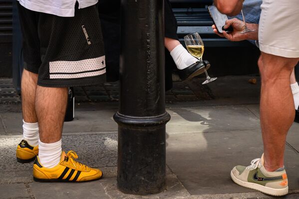 امرأة تحمل كأس نبيذ بحذائها، بينما تسترخي مع أصدقائها، في 3 يوليو 2025، لندن، المملكة المتحدة. وتشهد لندن حاليًا طقسًا دافئًا، ومن المتوقع أن تعود درجات الحرارة إلى 30 درجة مئوية، الأسبوع المقبل - سبوتنيك عربي