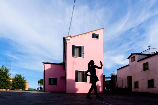 صورة ظلية لمرأة تلتقط صورة "سيلفي" أمام منزل مطلي باللون الوردي في جزيرة بورانو، إحدى جزر البندقية الـ118، إيطاليا. - سبوتنيك عربي