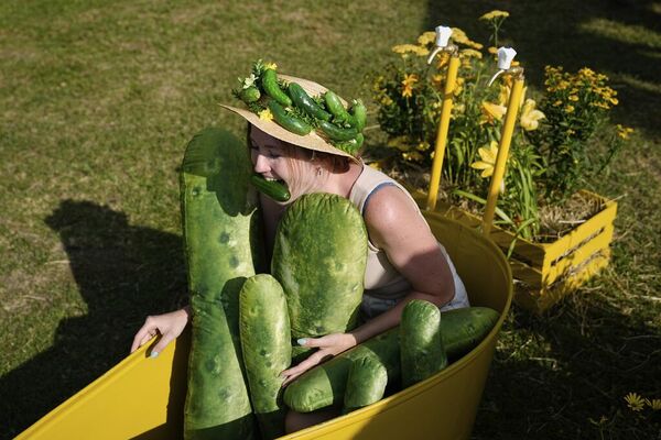 امرأة ترتدي قبعة مزينة بخيار بلاستيكي، وتقضم خيارة أثناء جلوسها في حوض غسيل مملوء بالخيار، في مهرجان الخيار في سوزدال، روسيا - سبوتنيك عربي