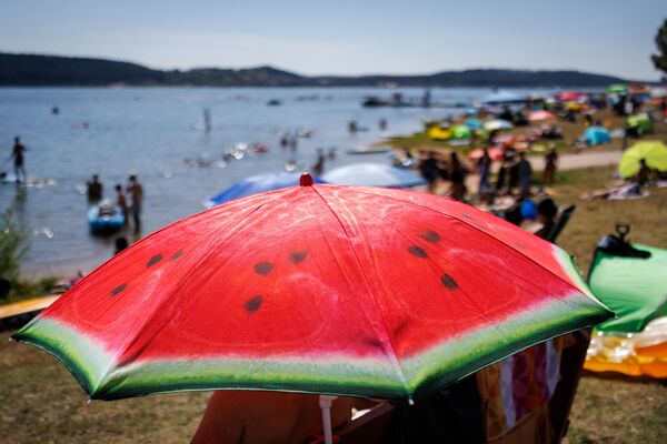 مظلة شمسية مطبوعة عليها بطيخة تقف على شاطئ بحيرة برومباخ المزدحم في يوم حار. - سبوتنيك عربي