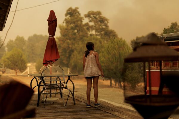 فتاة تراقب من شرفة منزلها رجال الإطفاء وهم يكافحون ألسنة اللهب من حريق كانيون في كاستايك، كاليفورنيا. - سبوتنيك عربي