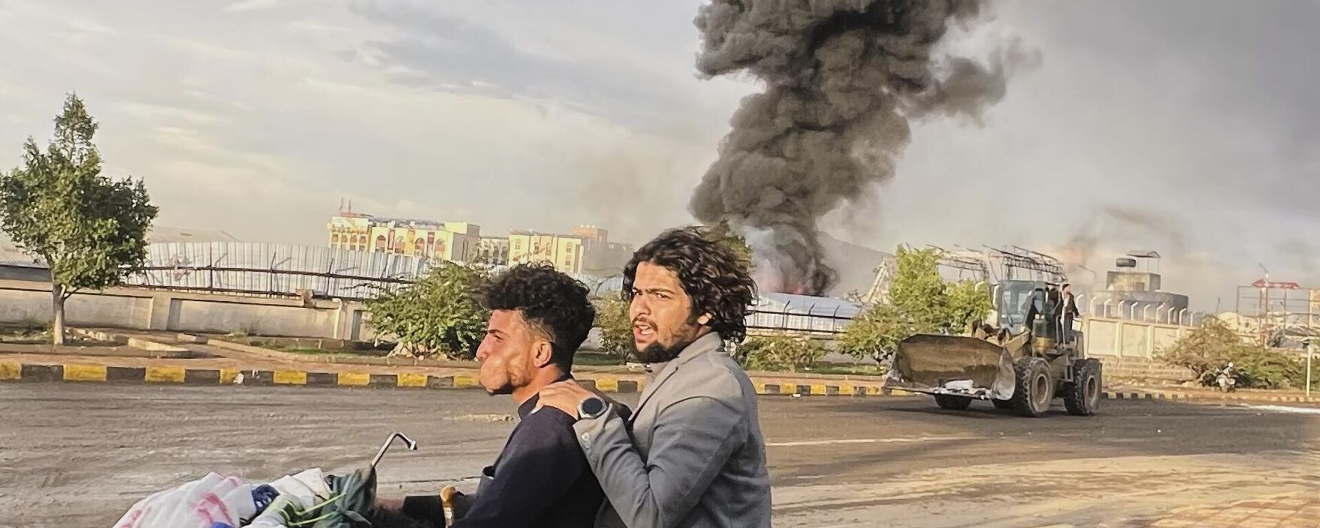 أشخاص يركبون دراجة نارية بينما يتصاعد الدخان في أعقاب الغارات الجوية الإسرائيلية على مناطق متعددة بما في ذلك محطة طاقة ومحطة وقود في صنعاء في اليمن. - سبوتنيك عربي, 1920, 28.09.2025