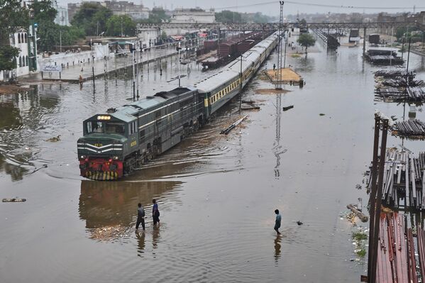 قطار ركاب يغادر محطة سكة حديد عبر مسارات غمرتها المياه بسبب الأمطار الغزيرة، في باكستان. - سبوتنيك عربي