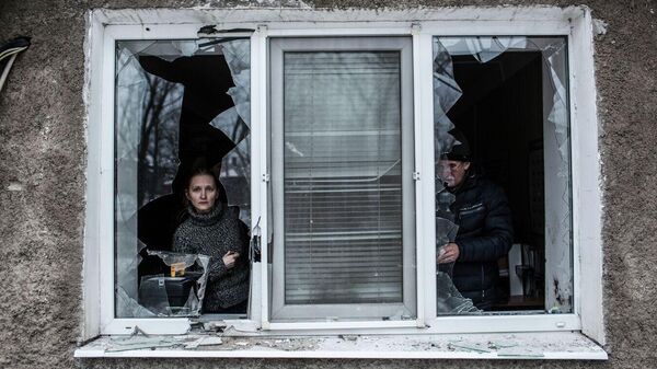 امرأة تنظر من خلال نافذة مكسورة في شقتها بعد قصفها بالمدفعية الأوكرانية في منطقة فوروشيلوفسكي وسط دونيتسك، أوكرانيا.  - سبوتنيك عربي
