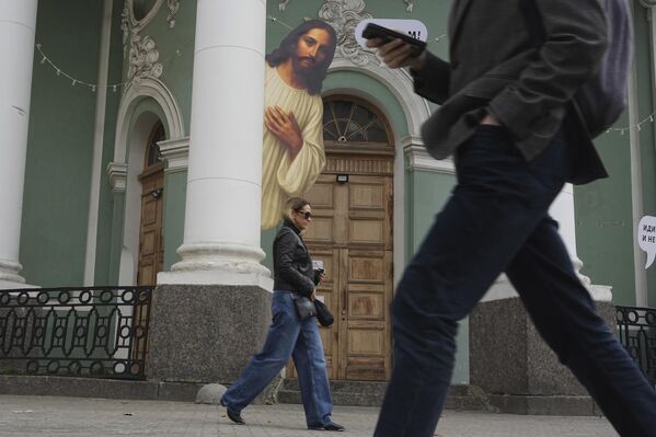 أشخاص يمرون أمام صورة يسوع المسيح المثبتة على عمود كنيسة "أنينكيرش" اللوثرية في سان بطرسبورغ، روسيا. - سبوتنيك عربي