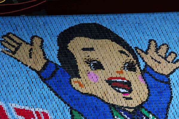 شكل المواطنون المشاركون في الاحتفال صورة طفل مبتسم ويرفع يديه، وذلك من خلال قيام عدد كبير من الجمهور المتواجدين على مدرجات الملعب بقلب بطاقات ملونة ورفعها إلى الأعلى. - سبوتنيك عربي