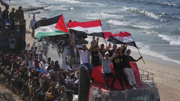 نازحون فلسطينيون يركبون شاحنات محملة بأمتعتهم ويلوحون بالأعلام المصرية والفلسطينية أثناء سفرهم على طول الطريق الساحلي بالقرب من وادي غزة في وسط قطاع غزة، متجهين نحو مدينة غزة - سبوتنيك عربي