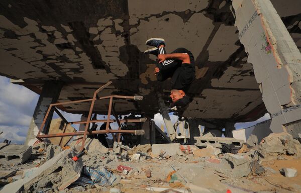 رياضيون فلسطينيون شباب يؤدون حركات باركور بين أنقاض المباني المدمرة في منطقة المغراقة، عقب وقف إطلاق النار في مدينة غزة.يستخدم الرياضيون رياضتهم للفت الانتباه إلى الدمار الذي خلفته الهجمات الإسرائيلية، مستعرضين مهاراتهم البهلوانية وسط الأنقاض. - سبوتنيك عربي