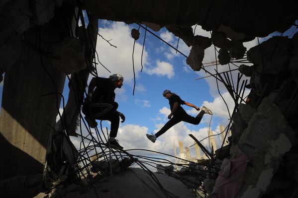 رياضيون فلسطينيون شباب يؤدون حركات باركور بين أنقاض المباني المدمرة في منطقة المغراقة، عقب وقف إطلاق النار في مدينة غزة.يستخدم الرياضيون رياضتهم للفت الانتباه إلى الدمار الذي خلفته الهجمات الإسرائيلية، مستعرضين مهاراتهم البهلوانية وسط الأنقاض. - سبوتنيك عربي