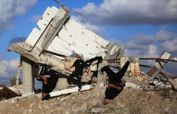 رياضيون فلسطينيون شباب يؤدون حركات باركور بين أنقاض المباني المدمرة في منطقة المغراقة، عقب وقف إطلاق النار في مدينة غزة.يستخدم الرياضيون رياضتهم للفت الانتباه إلى الدمار الذي خلفته الهجمات الإسرائيلية، مستعرضين مهاراتهم البهلوانية وسط الأنقاض. - سبوتنيك عربي