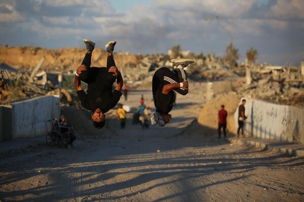 رياضيون فلسطينيون شباب يؤدون حركات باركور بين أنقاض المباني المدمرة في منطقة المغراقة، عقب وقف إطلاق النار في مدينة غزة.يستخدم الرياضيون رياضتهم للفت الانتباه إلى الدمار الذي خلفته الهجمات الإسرائيلية، مستعرضين مهاراتهم البهلوانية وسط الأنقاض. - سبوتنيك عربي