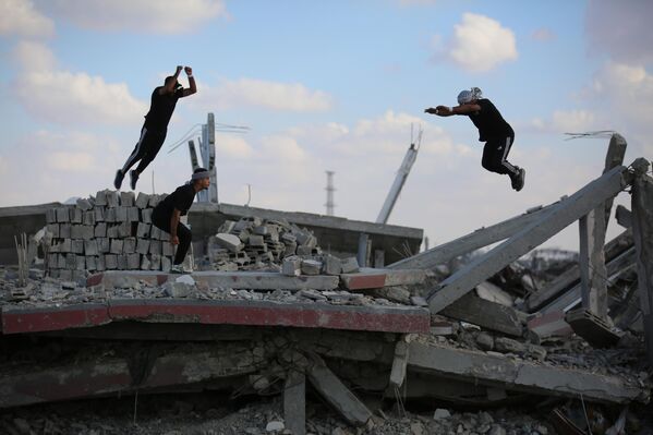 رياضيون فلسطينيون شباب يؤدون حركات باركور بين أنقاض المباني المدمرة في منطقة المغراقة، عقب وقف إطلاق النار في مدينة غزة.يستخدم الرياضيون رياضتهم للفت الانتباه إلى الدمار الذي خلفته الهجمات الإسرائيلية، مستعرضين مهاراتهم البهلوانية وسط الأنقاض. - سبوتنيك عربي