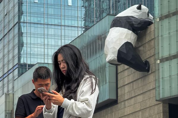 مشاة يتفقدون هواتفهم الذكية بالقرب من تمثال الباندا العملاق الشهير على الجدار الخارجي لمركز التسوق "ساحة تشنغدو المالية الدولية"، أحد معالم المدينة الشهيرة. - سبوتنيك عربي