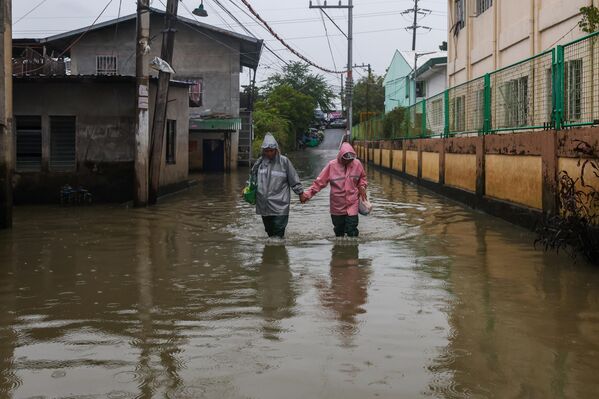 زوجان يخوضان طريقهما عبر شارع غمرته المياه بسبب إعصار "فونغ وونغ" الذي جلب رياحًا عاتية وأمطارًا غزيرة. - سبوتنيك عربي