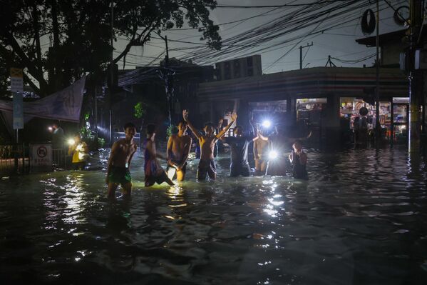 بعض من الشباب المتطوعين يقومون بتوجبه حركة المركبات عبر شوارع غمرتها مياه الفيضانات، وسط انقطاع التيار الكهربائي. - سبوتنيك عربي