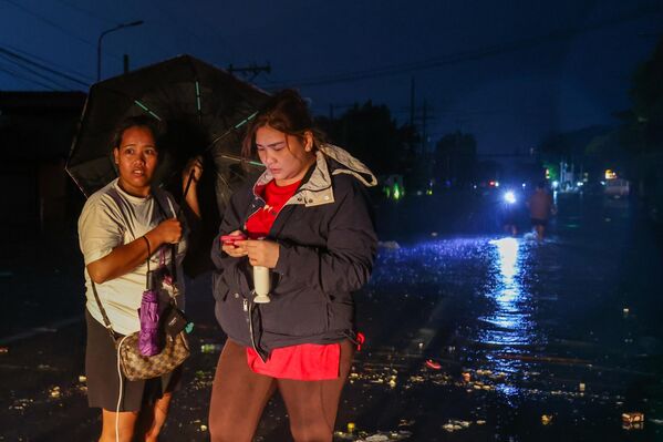فتاتان تنتظران انحسار المياه، في منطقة غمرتها الفيضانات، وسط انقطاع للتيار الكهربائي. - سبوتنيك عربي
