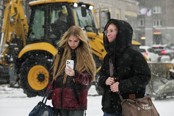 فتاتان في أحد شوارع نوفوسيبيرسك أثناء تساقط الثلوج، وقيام الاَليات بإزالة الثلوج المتراكمة على الطريق. - سبوتنيك عربي