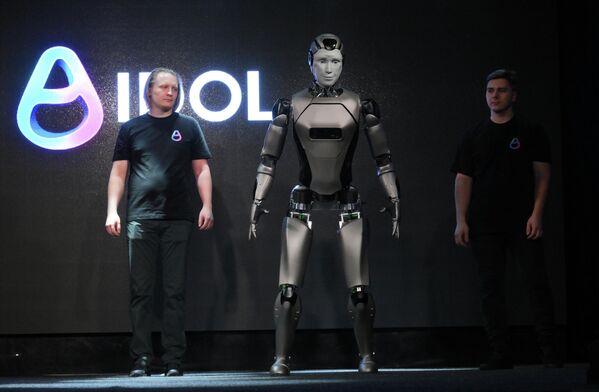 صورة تظهر الروبوت &quot;أيدول&quot; واقفًا على المسرح، محاطًا بأشخاص عدة. ويبرز في الصورة حجم الروبوت وشكله الكامل. - سبوتنيك عربي
