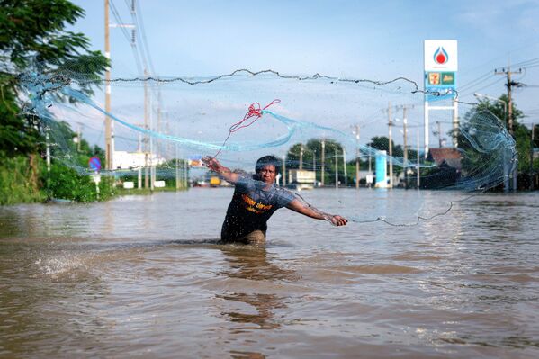 سكان محليون متضررون من الفيضانات يرمون شباك صيد (دراي) على الطريق السريع 33، في مقاطعة باموك، المغلقة مؤقتًا بسبب غمر الطريق السريع بمياه الفيضانات، تايلاند - سبوتنيك عربي