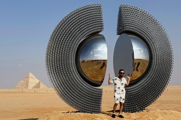 زائر يقف بجانب عمل &quot;الشن&quot;، للفنان التركي ميرت آغي كوس، خلال النسخة الخامسة من معرض &quot;إلى الأبد الآن&quot;، للفن المعاصر في موقع أهرامات الجيزة التاريخي، مصر - سبوتنيك عربي