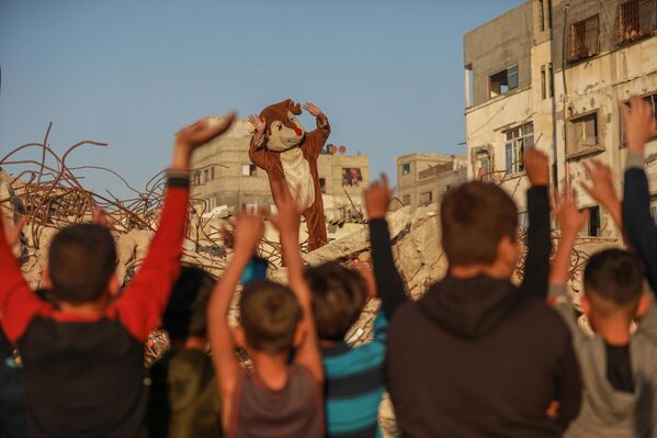  مجموعة من المتطوعين الفلسطينيين  يرتدون أزياء تنكرية، بين أنقاض المباني المدمرة في مخيم الشاطئ لللاجئين، خلال تنظيم فعالية ترفيهية للأطفال في غزة. - سبوتنيك عربي