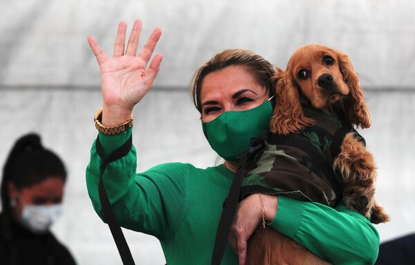 رئيسة بوليفيا المؤقتة جانين أنيز، ترتدي قناعًا وسط جائحة فيروس الجديد، تحمل كلبها أثناء تحيتها للناس خلال إعلان عن إنشاء ملجأ للحيوانات المهجورة في لاباز، بوليفيا، الأحد 20 سبتمبر/أيلول 2020. - سبوتنيك عربي