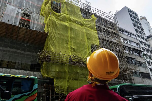 عامل بناء يقف بالقرب من مبنى قيد التجديد في منطقة هونغ كونغ وينظر باتجاه الأعلى. - سبوتنيك عربي