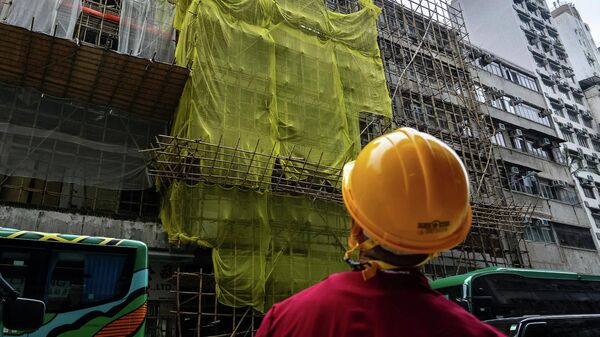 Рабочий-строитель стоит возле ремонтируемого здания в районе Монг Кок после пожара, Гонконг - سبوتنيك عربي